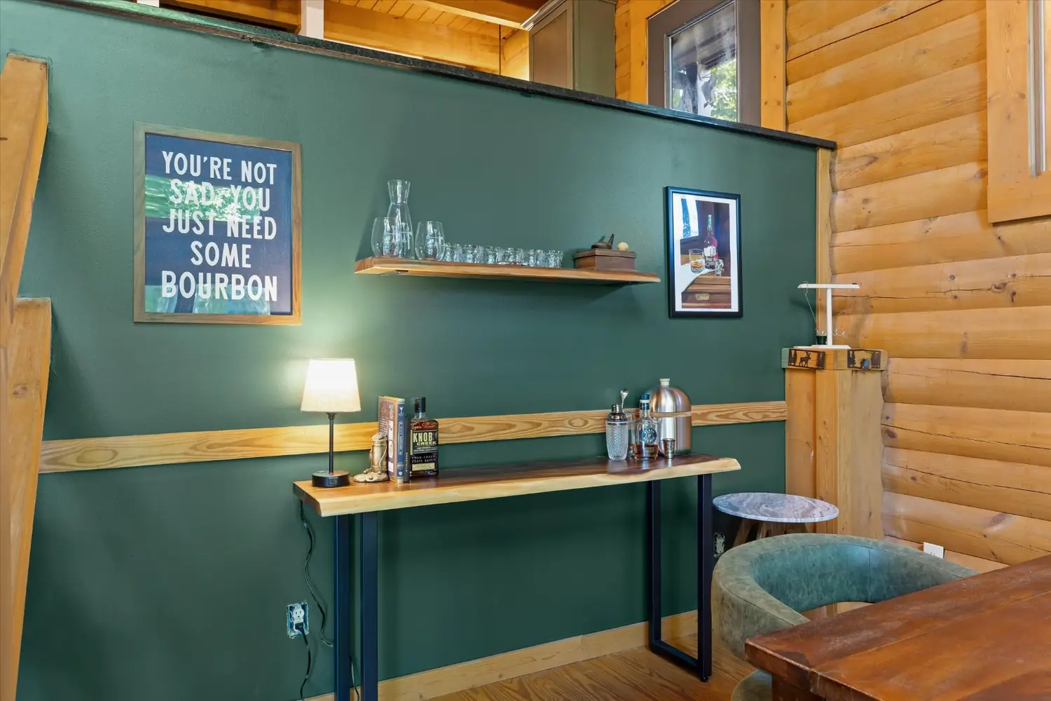 Built-in bar with open shelving, bottles, and a framed bourbon sign on a green wall
