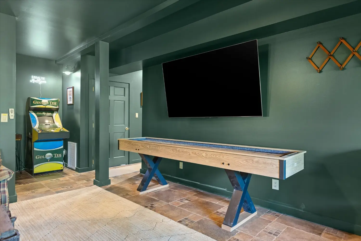 Full length shuffleboard table in a green paneled room with a mounted television